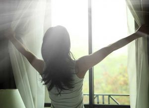 Woman opening the curtains to reveal the sunshine